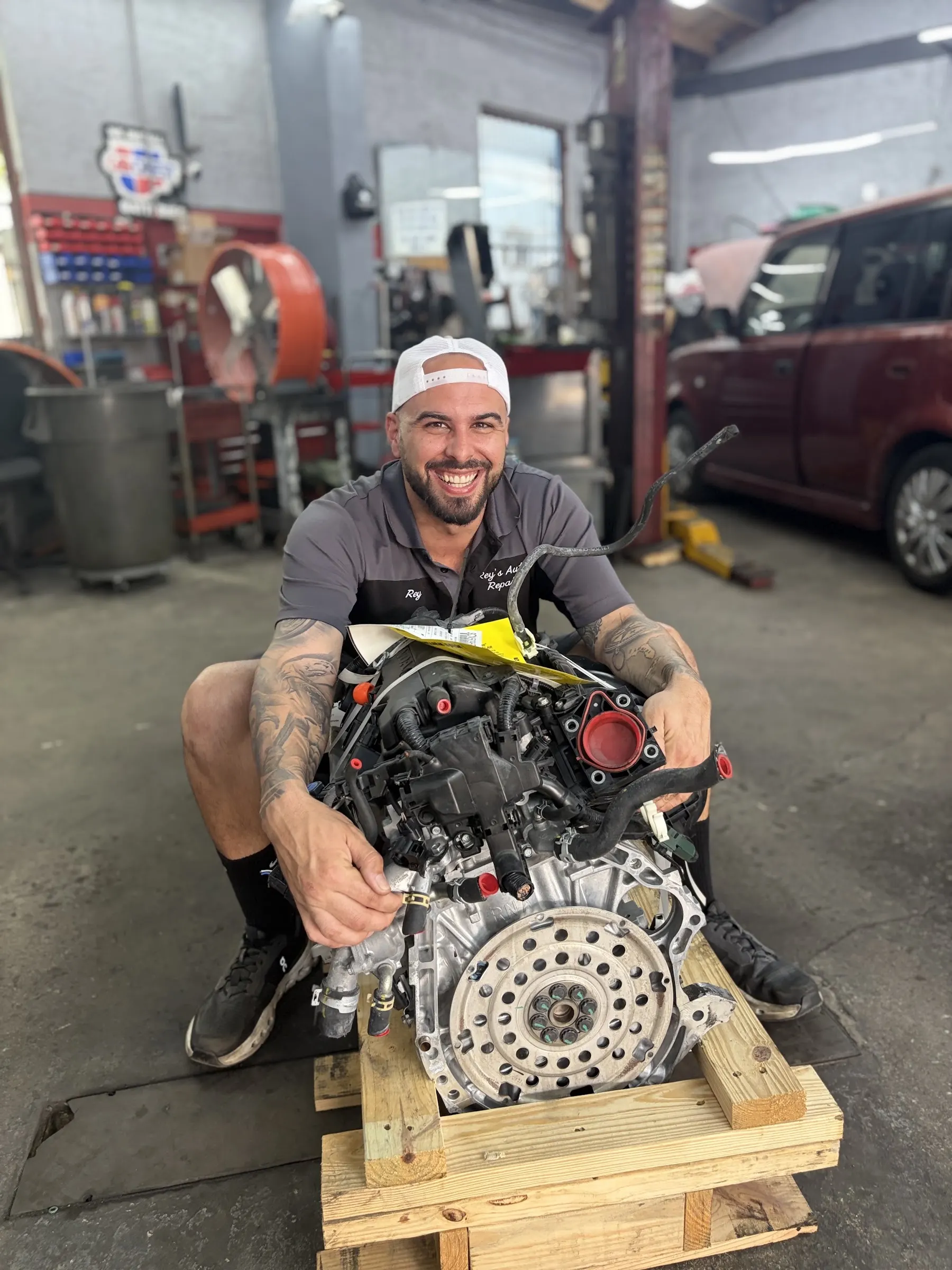 Mechanic smiling with an engine on the shop floor at Rey's Auto Repair